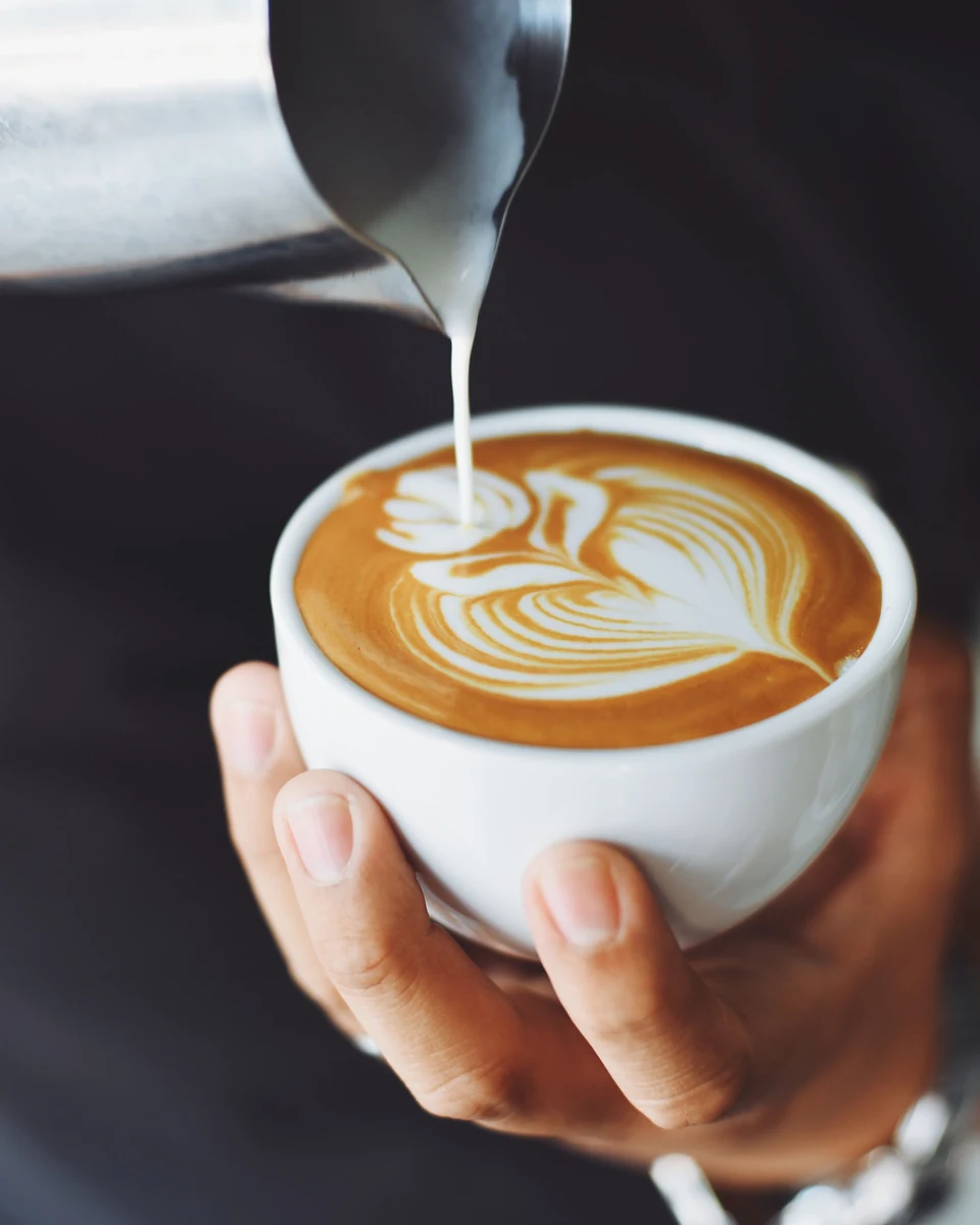 Milchschaum wird von Hand zu Latte Art in eine Cappuccinotasse gegossen.